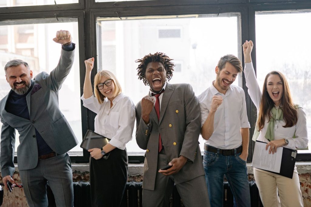 Services A joyful, diverse group of colleagues celebrating success indoors with cheerful expressions.